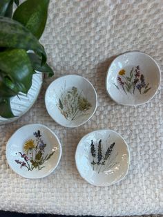 four white bowls with flowers painted on them sitting next to a potted plant and rug