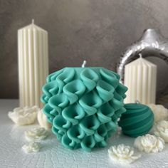 a teal colored candle sitting on top of a table next to some white flowers