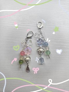 three charms are sitting on a table with hearts and flowers in the background, one has a dangling charm