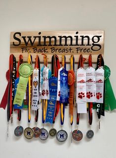 there are many medals hanging on the wall next to each other and one has a plaque that says swimming