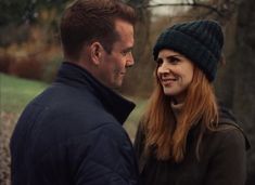 a man and woman standing next to each other in front of trees with leaves on the ground