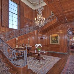 an ornate staircase with chandelier and wooden paneling in a large room filled with potted plants