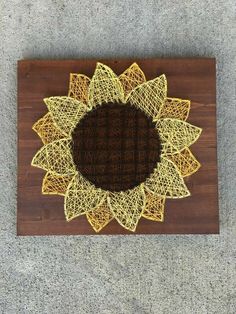 a string art sunflower on a wooden board with brown and yellow yarn around it