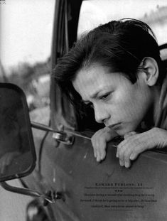 a black and white photo of a man leaning out the window of a car looking at something