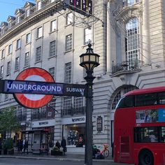 a red double decker bus driving past a tall building