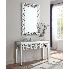 a white console table with a mirror and vase on it in front of a window