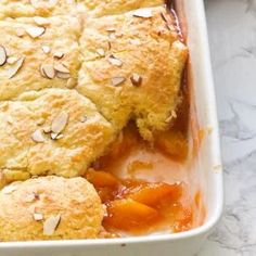 a casserole dish filled with peach cobbler and topped with sliced almonds