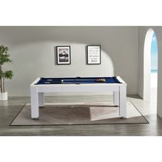 a white pool table with blue cloth on the top and two framed pictures above it