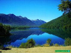 a lake surrounded by mountains and trees in the middle of a green valley with blue water