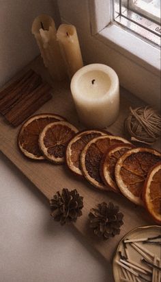 an assortment of dried oranges on a cutting board next to a candle and some pine cones