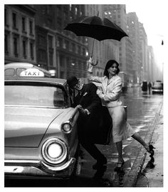 a man and woman standing on the side of a street holding an umbrella