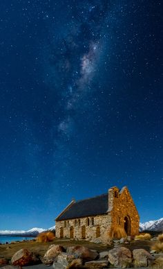 an old church sits on the side of a mountain under a night sky filled with stars