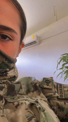 a woman in camouflage is holding something up to her face and looking at the camera