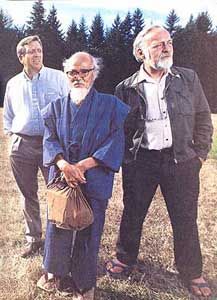 three older men standing next to each other on a field with trees in the background