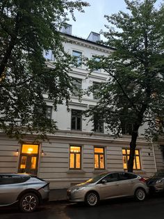 two cars are parked in front of a building at night with the sun shining through the windows