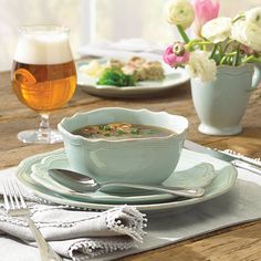 a bowl of soup sits on a table with silverware and flowers in the background