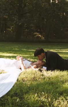 a man and woman laying in the grass on top of a white cloth covered blanket