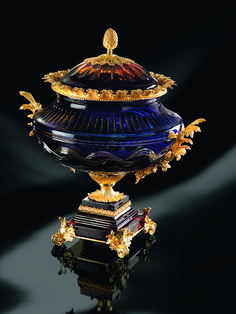 an ornate blue vase with gold decoration on it's top and bottom, sitting on a reflective surface