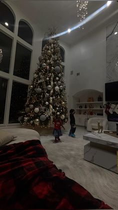 a living room with a christmas tree in the corner and two children standing near it