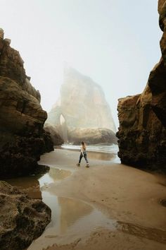 a person walking on the beach near some rocks