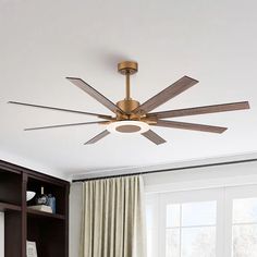 a ceiling fan in a living room next to a book shelf and window with curtains