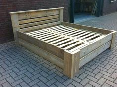 a wooden bed frame sitting on top of a brick floor