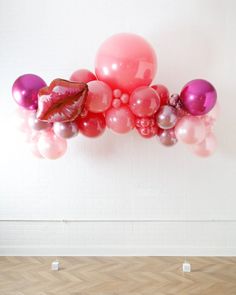 a bunch of balloons floating in the air on a wooden floor next to a brick wall