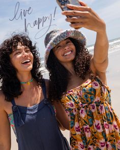 two women standing on the beach taking a selfie with a cell phone that says live happy