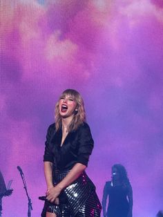 the singer is singing on stage with her hands in her pockets as she stands next to two other performers