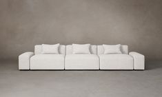 a white couch sitting on top of a gray floor next to a wall with pillows