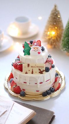 a three tiered cake decorated with berries and santa clause on top, sitting on a gold platter