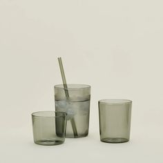 three glass cups and one cup with a straw sticking out of the top, sitting on a white surface