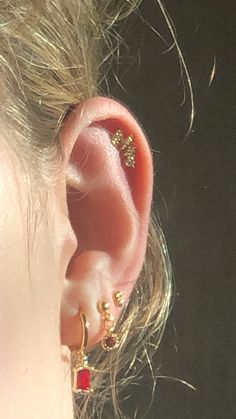 a close up of a person's ear wearing gold earrings with red stones on them