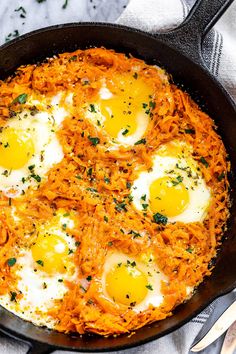 three eggs are in a skillet with shredded carrots and parsley on the side