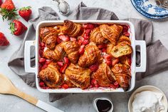 strawberry croissants and whipped cream in a white casserole dish with strawberries on the side