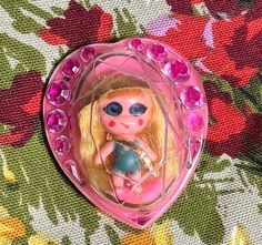 a small doll with blue eyes and blonde hair in a pink heart - shaped box