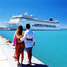 two people standing on a dock looking at a cruise ship