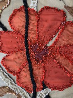 a red flower with sequins on it sitting on top of a piece of cloth