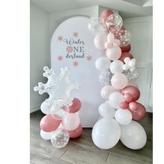 the balloon arch is decorated with pink, white and silver balloons for a winter onederant party