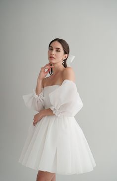 a woman in a white dress posing for the camera with her hand on her cheek