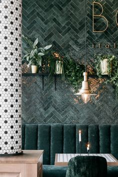 a restaurant with green velvet booths and plants on the wall, along with two candles