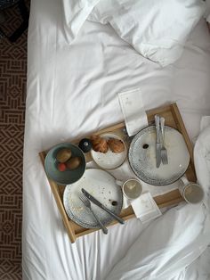 a tray with plates and silverware on top of a white bed in a hotel room