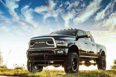 a large black truck parked on top of a lush green field under a blue cloudy sky