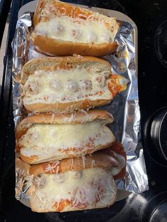 four hotdogs covered in cheese and sauce sitting on top of foil lined up