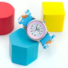 a pink and blue watch sitting on top of a wooden block next to colorful blocks