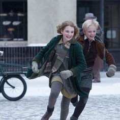 two girls are playing in the snow on a city street while one girl is holding onto her coat