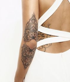 the back of a woman's white dress with tattoos on her arm and shoulder