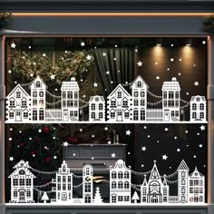 a christmas window display with white paper cut out houses and trees in the windowsill