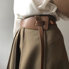 a woman wearing a white shirt and tan skirt with a brown belt on her waist