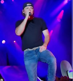 a man in black shirt and jeans on stage singing into microphone with blue lights behind him